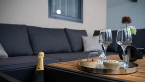 Uma sala de estar moderna com um sofá cinza escuro, uma mesa de centro de madeira, uma garrafa de champanhe, dois copos e um objeto decorativo.