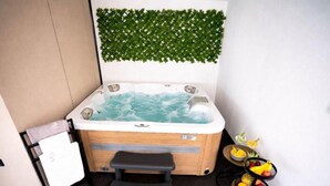 Uma banheira de hidromassagem com exterior de madeira, um pequeno degrau para entrar e uma decoração de folhagem verde fixada na parede.