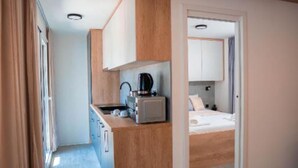 Quarto compacto com cozinha compacta, uma cama e porta que dá para outro quarto.