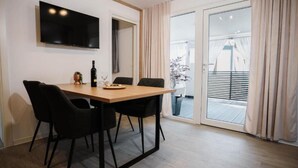 A modern dining area with a wooden table and black chairs, a flat-screen TV mounted on the wall, and a sliding glass door leading to an outdoor balcony. - Lux Mobile Homes Vodice - Two bedroom home with private hot tub (Aurora) (Vodice)