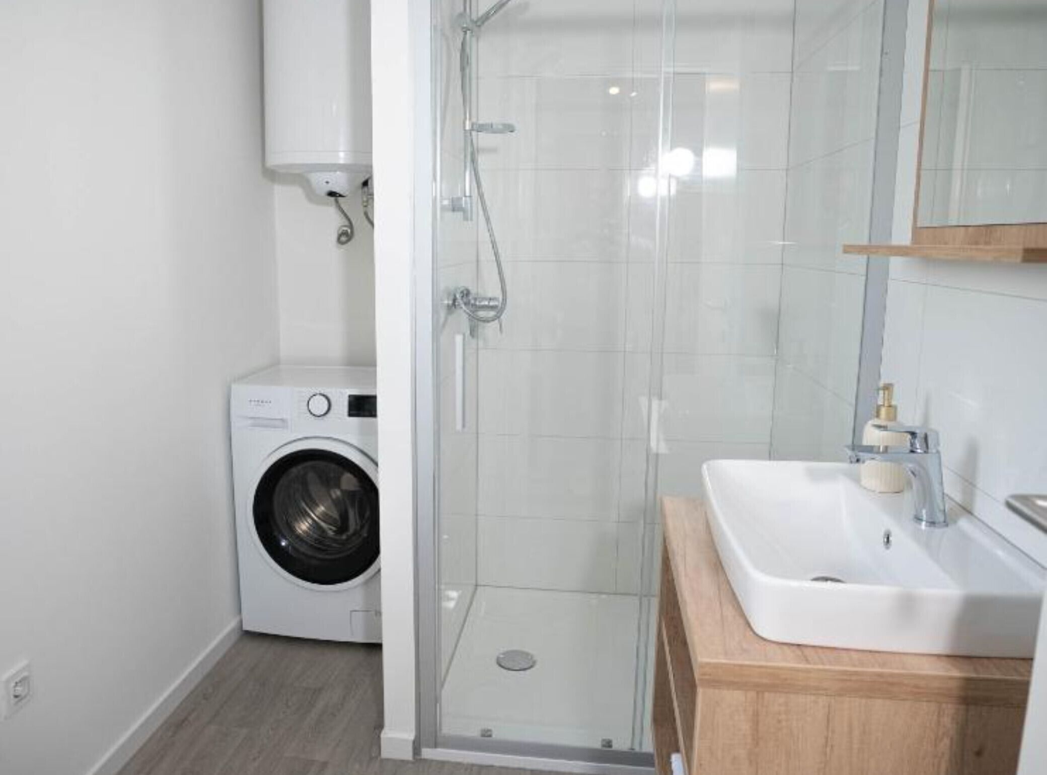 Un baño moderno con cabina de ducha de vidrio, lavadora integrada y tocador de madera con lavabo.