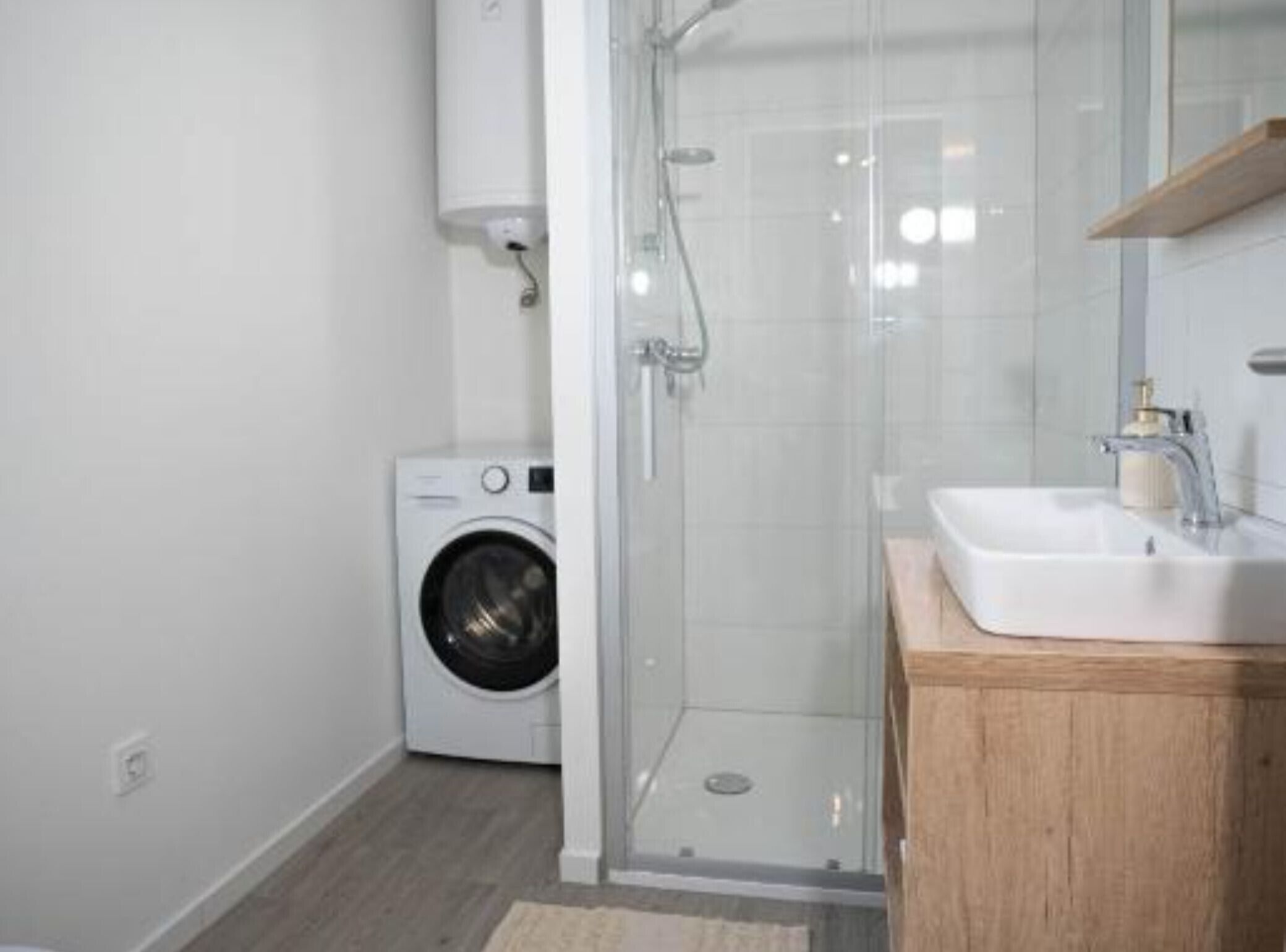 A modern bathroom with a glass shower enclosure, a built-in washing machine, and a wooden vanity with a sink.