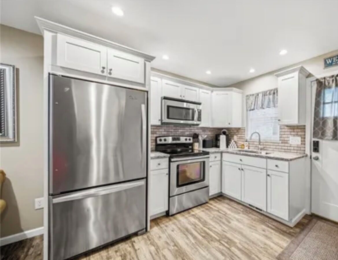 A modern kitchen with stainless steel appliances, white cabinetry, and a herringbone-patterned backsplash.