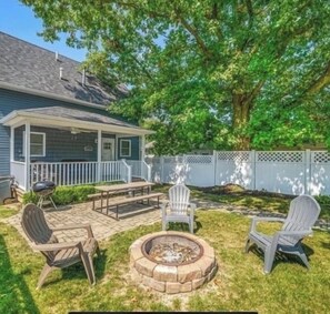 Ein Garten mit überdachter Terrasse, Feuerstelle und Gartenmöbeln.