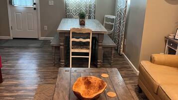Un comedor con mesa de madera, sillas, lámpara colgante y un reloj en la pared.
