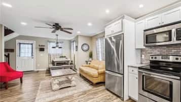 Una cocina moderna con electrodomésticos de acero inoxidable, una zona de comedor con una silla roja y una sala de estar con un sofá color beige.