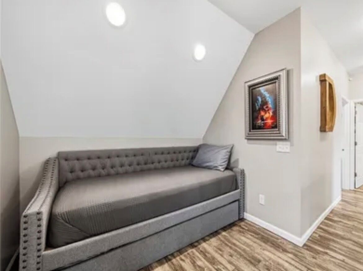 Un dormitorio tipo loft con sofá gris, un cuadro enmarcado en la pared y suelo de madera.