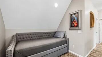 Un dormitorio tipo loft con sofá gris, un cuadro enmarcado en la pared y suelo de madera.