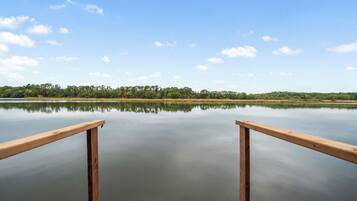 Un molo di legno che si protende in acque calme sotto un cielo sereno, con una riva alberata.