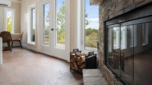 Una habitación con ventanas amplias, una chimenea de piedra y un montón de leña.