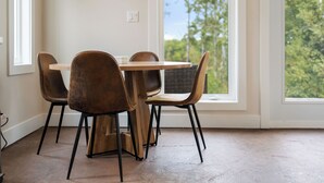 Un comedor con mesa y sillas, ventanas amplias y vistas a árboles.