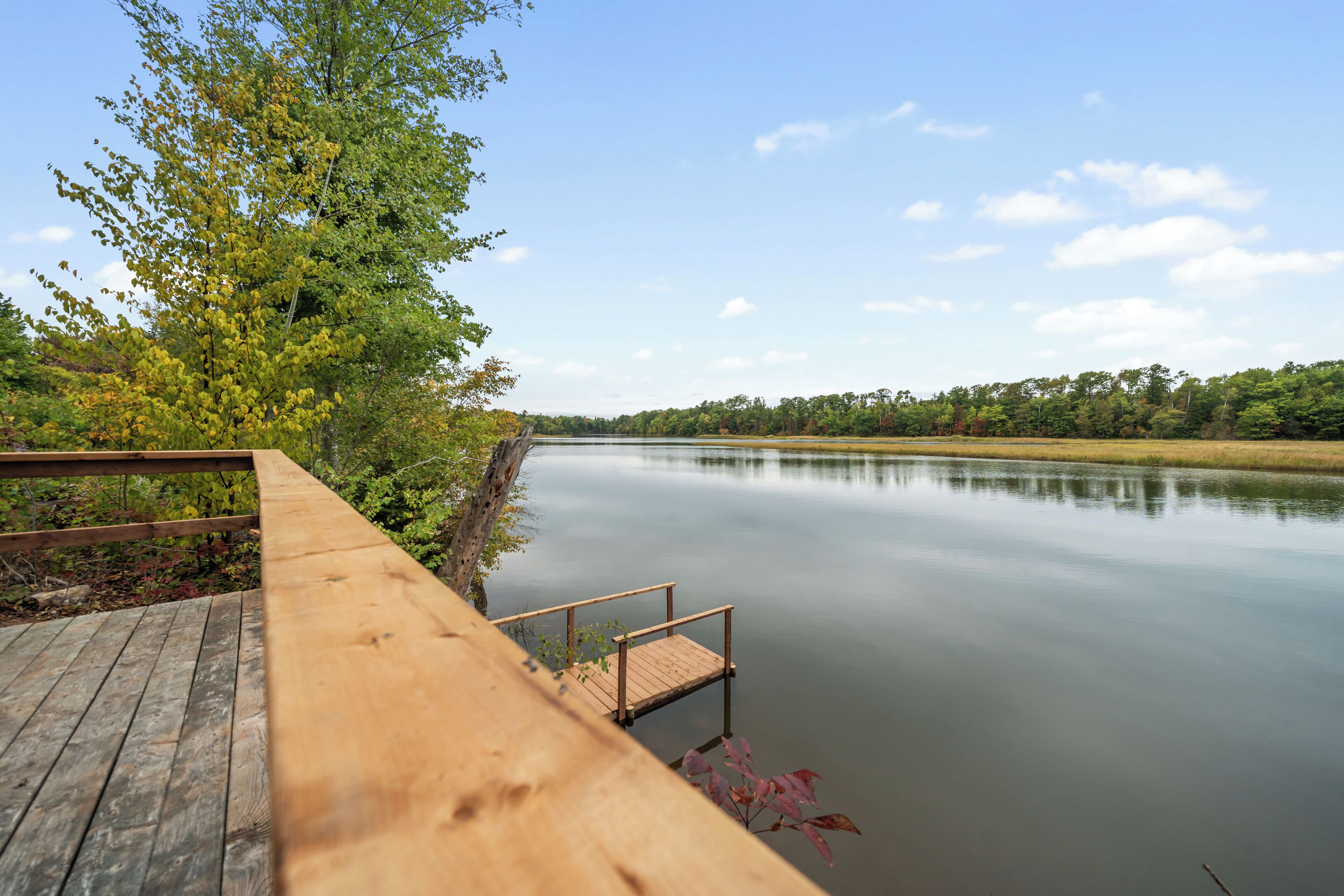 Une terrasse en bois s’étendant au-dessus d’un lac paisible, sous un ciel dégagé.