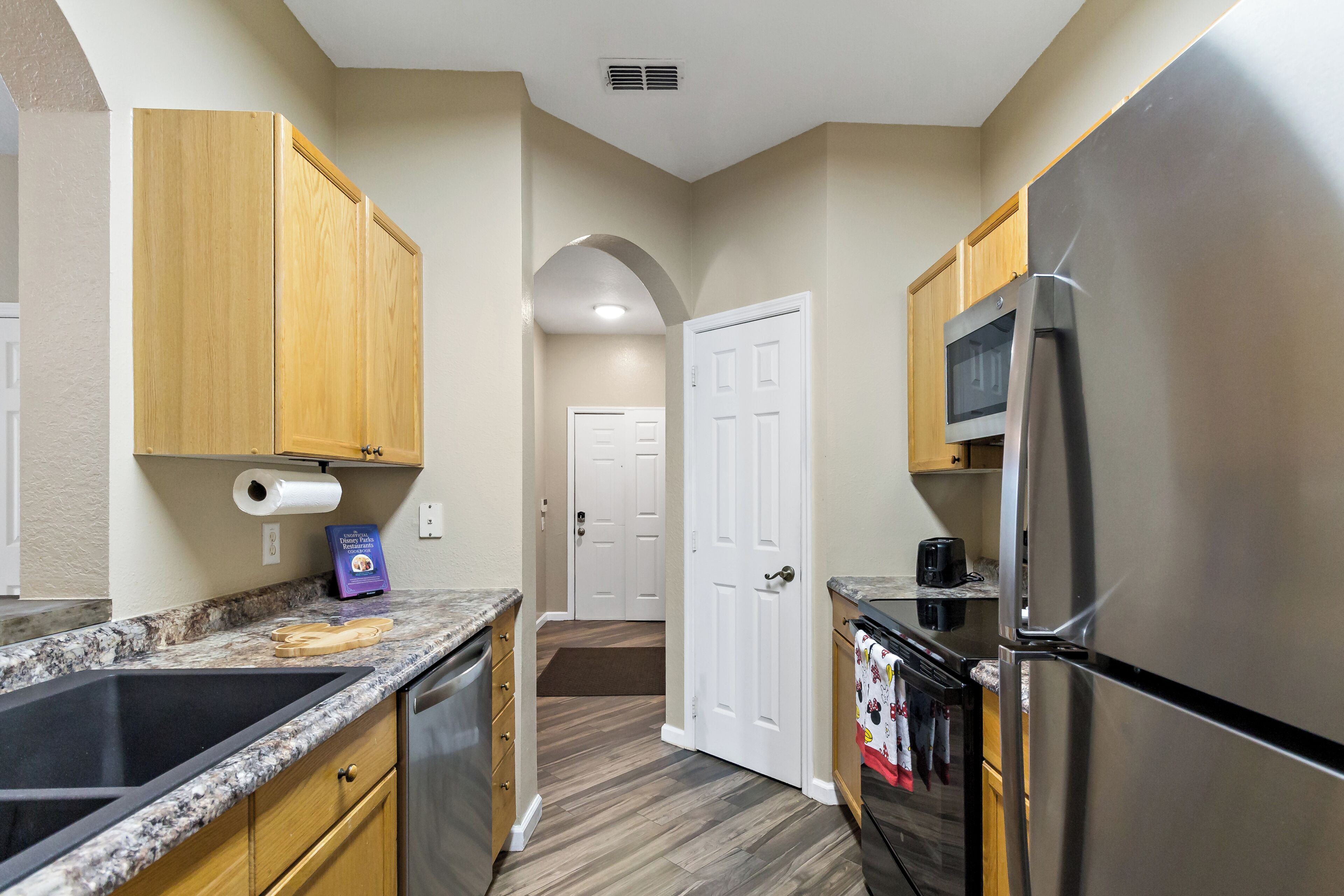 A kitchen with wooden cabinets, a stainless steel refrigerator, a microwave, and a granite countertop.