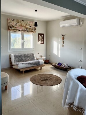 A modern living room with a sofa, a round rug, a small table, and a wall-mounted air conditioner.