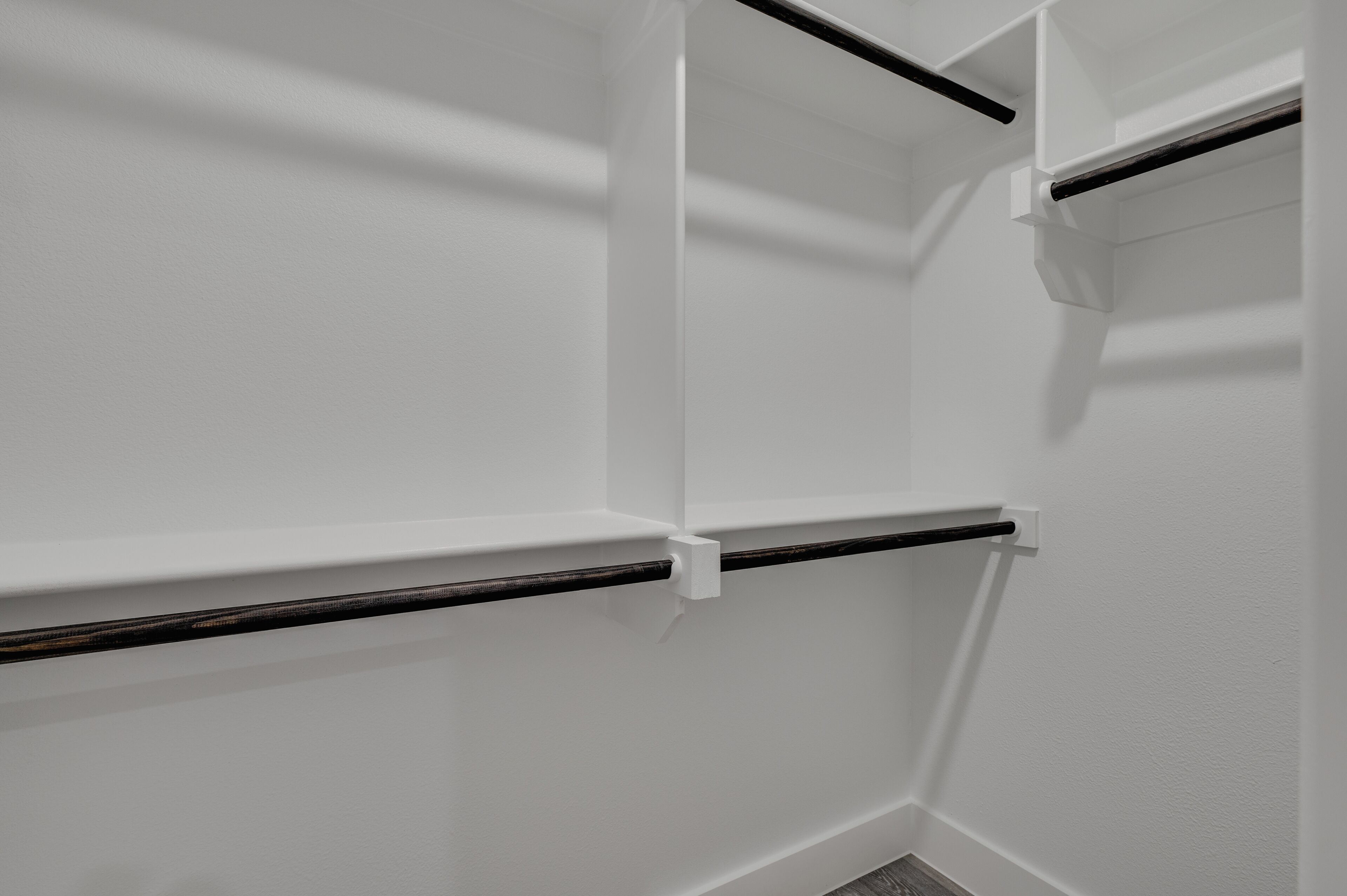 Een hoek van een kamer met witte muren en een zwarte horizontale stang, mogelijk een handdoekhouder.