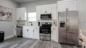 Una cocina moderna con armarios blancos, electrodomésticos de acero inoxidable y piso de madera gris.