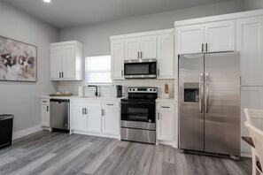 A modern kitchen with white cabinets, stainless steel appliances, and a grey wooden floor. - Brand New Duplex Near Downtown! (Greenville)