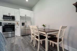 A modern kitchen with white cabinets, stainless steel appliances, and a wooden dining table with chairs. - Brand New Duplex Near Downtown! (Greenville)