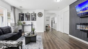 A modern living room with a sofa, coffee table, and fireplace. There is a kitchen in the background and a TV mounted on the wall. - Cozyluxstays FIFA World Cup Stay  Luxury 2BR + Game Room Near MetLife Stadium (Belleville)