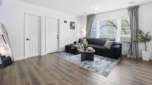 A modern living room with a dark sofa, a coffee table, and a large window with curtains. - Cozyluxstays FIFA World Cup Stay  Luxury 2BR + Game Room Near MetLife Stadium (Belleville)