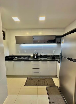 Eine moderne Küche mit weißen Schränken, einem Edelstahl-Kühlschrank, einem Gasherd und einer Mikrowelle.