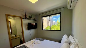 Habitación de hotel con cama, televisor montado en la pared, ventana con vista a la ciudad y equipo de aire acondicionado.
