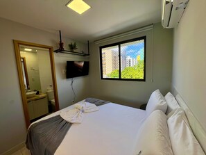 Ein Hotelzimmer mit Bett, Wandfernseher, Fenster mit Blick auf die Stadt und Klimaanlage.