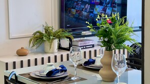 Un comedor con una mesa dispuesta para dos personas, un televisor mostrando la interfaz de Netflix y plantas decorativas.
