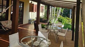 Un espacio de estar al aire libre cubierto con una mesa redonda de vidrio y sillas de mimbre blanco.