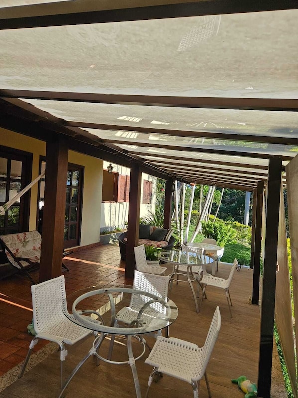 A covered outdoor seating area with a round glass table and white wicker chairs.