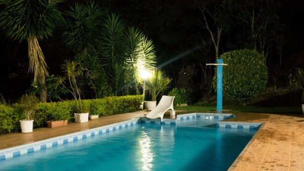 Una piscina con tobogán, rodeada de plantas en macetas y árboles.