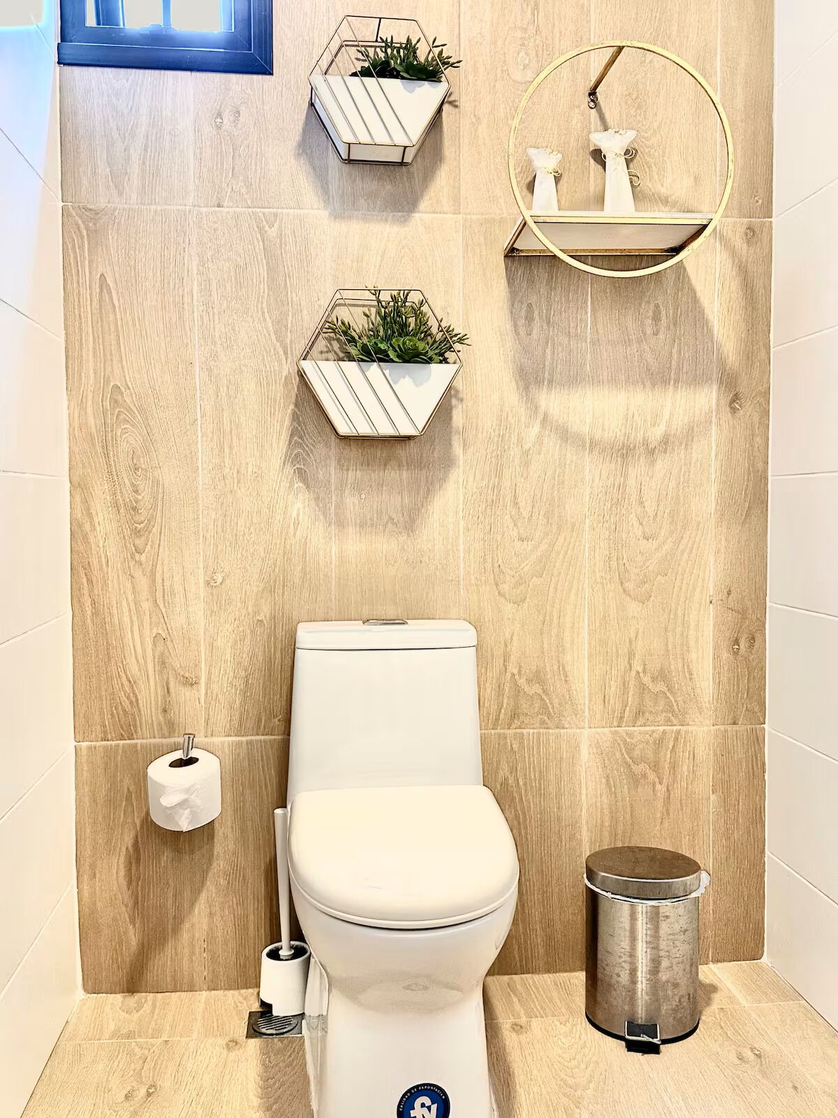A bathroom with a toilet, a trash can, and two wall-mounted planters with plants.