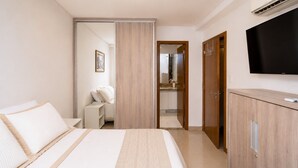 Une chambre d’hôtel avec un lit, une armoire, une télévision et une salle de bain visible à travers une porte ouverte.