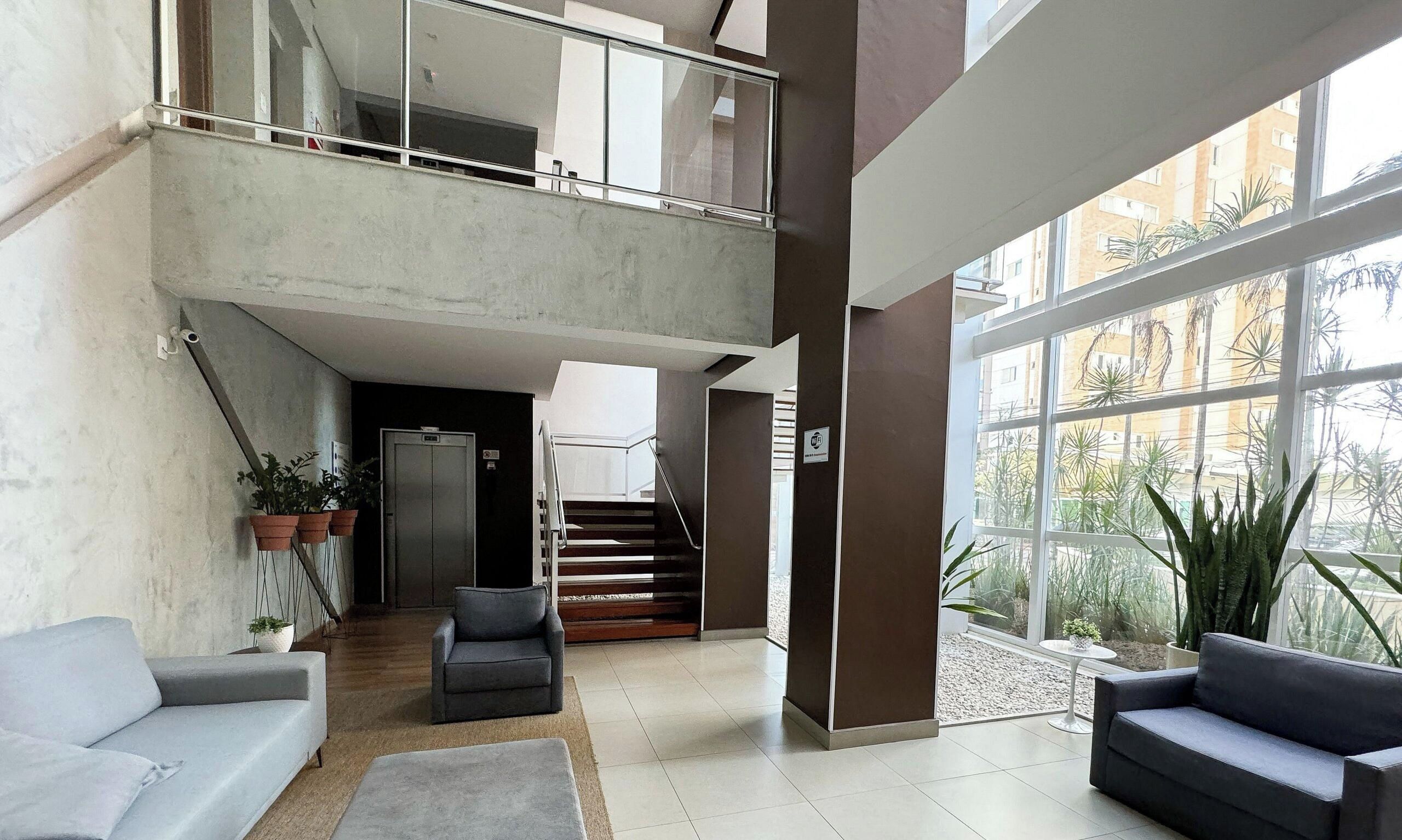 A spacious lobby with a staircase leading to an upper level, a grey sofa, and potted plants.