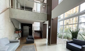 Un vestíbulo amplio con una escalera que conduce a un nivel superior, un sofá gris y plantas en macetas.