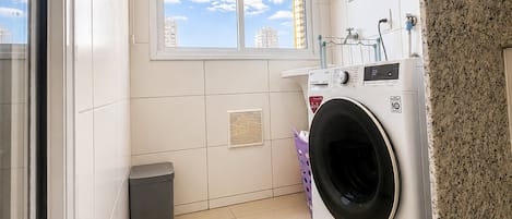 Un lavadero con lavadora, secadora, ventana con vista a edificios y suelo de baldosas.