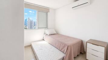 Un dormitorio con cama, mesita de noche, ventana con persianas y unidad de aire acondicionado.