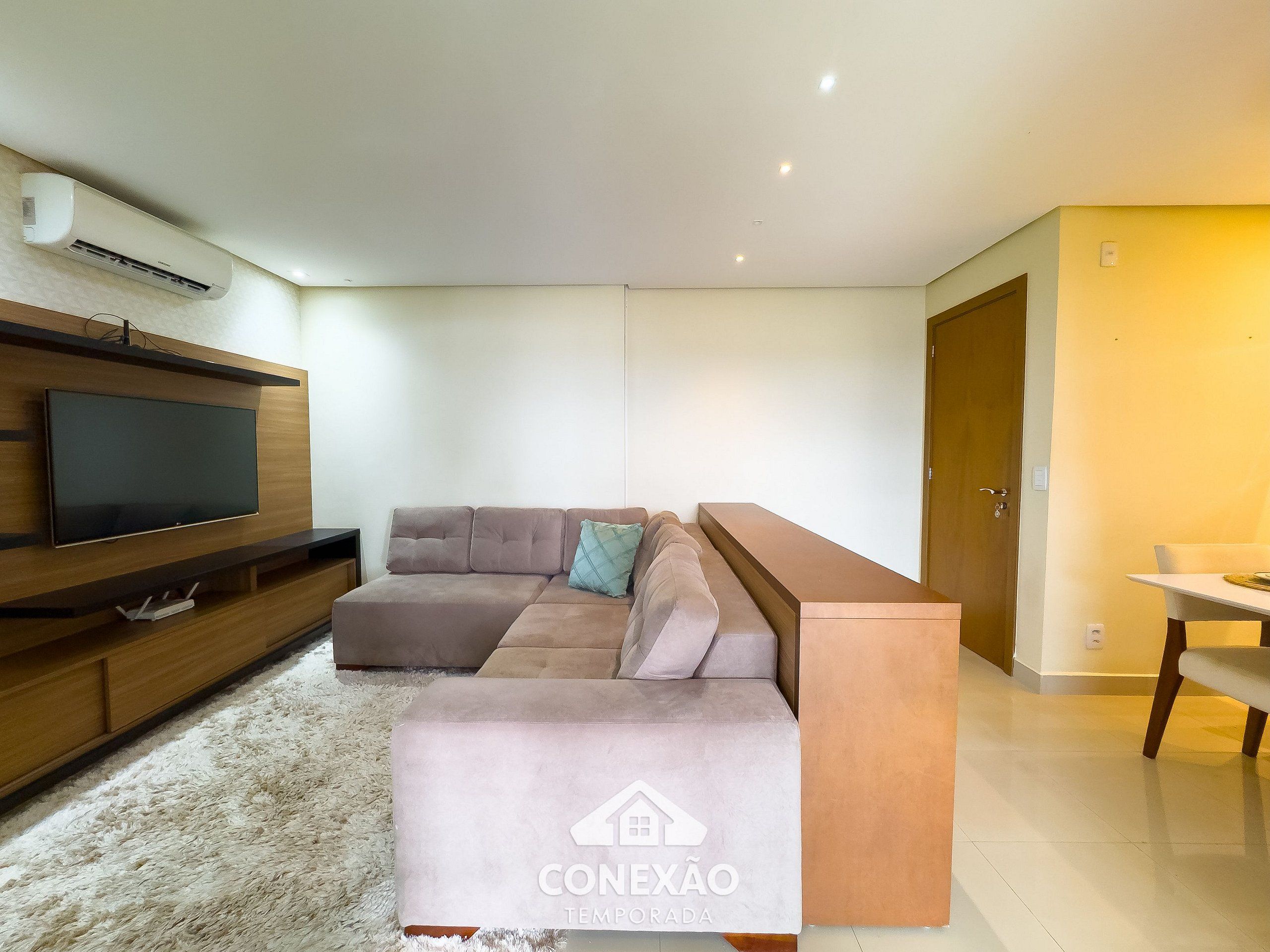 A modern living room with a sectional sofa, a flat-screen TV, and a wooden entertainment unit.