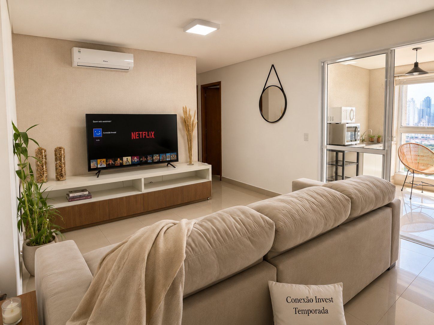 A modern living room with a flat-screen TV, a sofa, a coffee table, and a view of the city through a glass door.