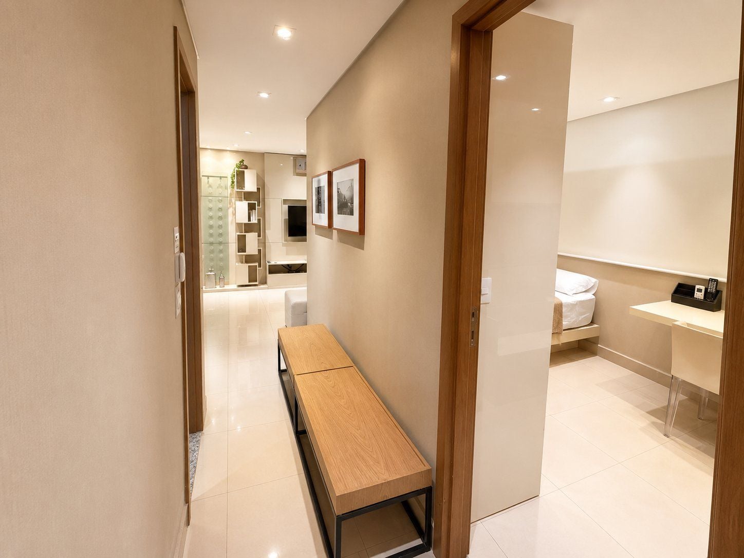 Una habitación de hotel moderna con un banco de madera, una mesita de noche y un escritorio pequeño con teléfono.