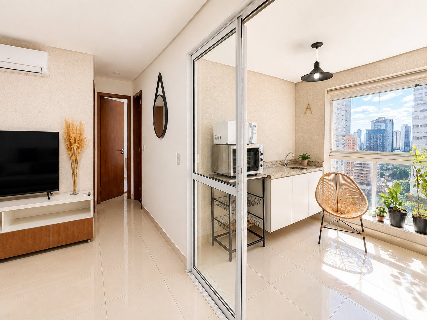 Una cocina moderna con microondas, horno y lavabo, un comedor con una silla y un televisor sobre un mueble.