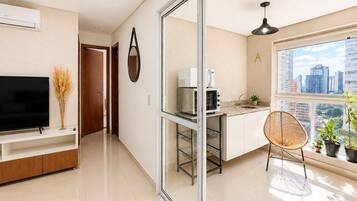 Una cocina moderna con microondas, horno y lavabo, un comedor con una silla y un televisor sobre un mueble.