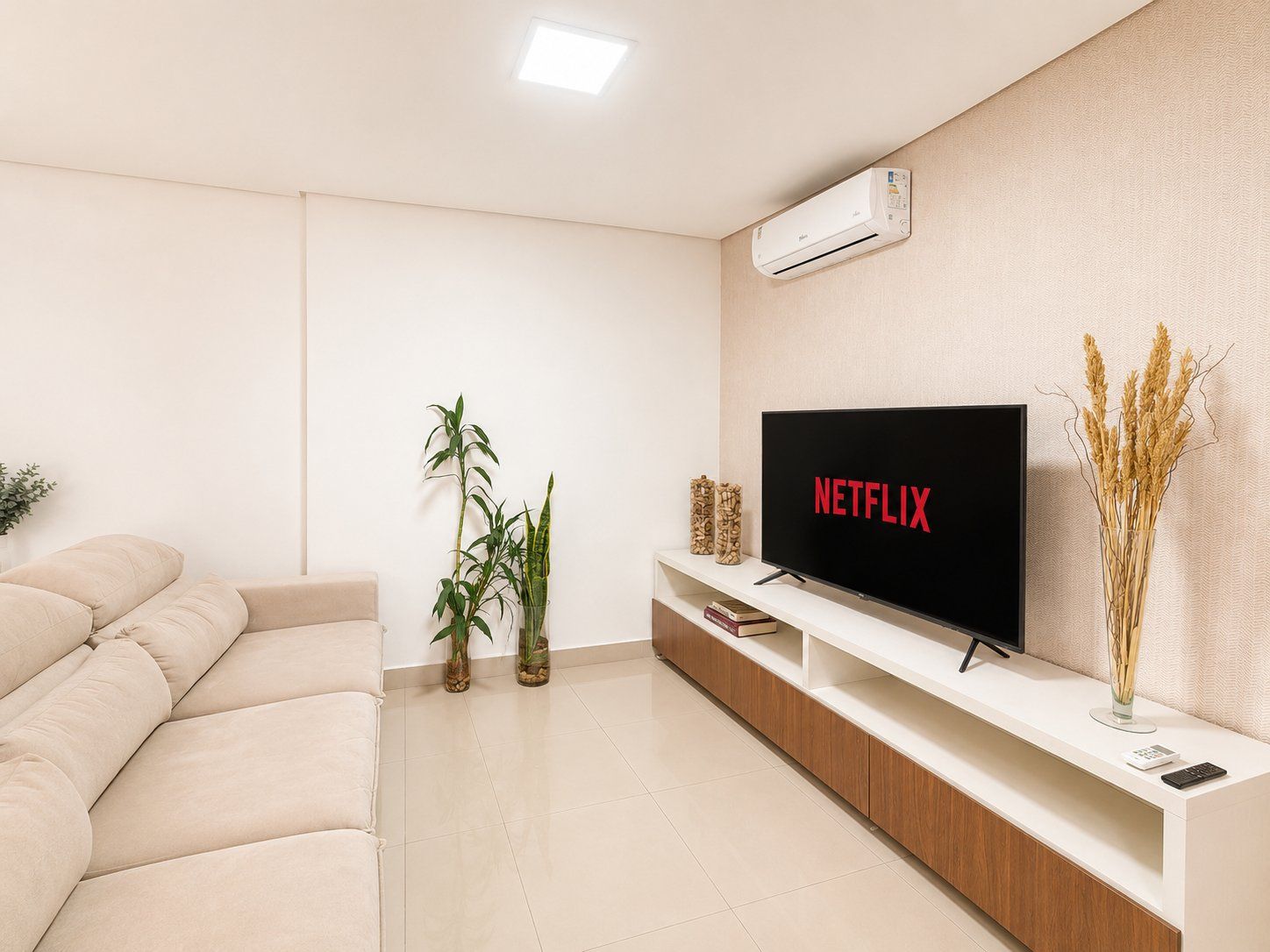 A modern living room with a flat-screen TV, a sofa, a plant, and a decorative vase.