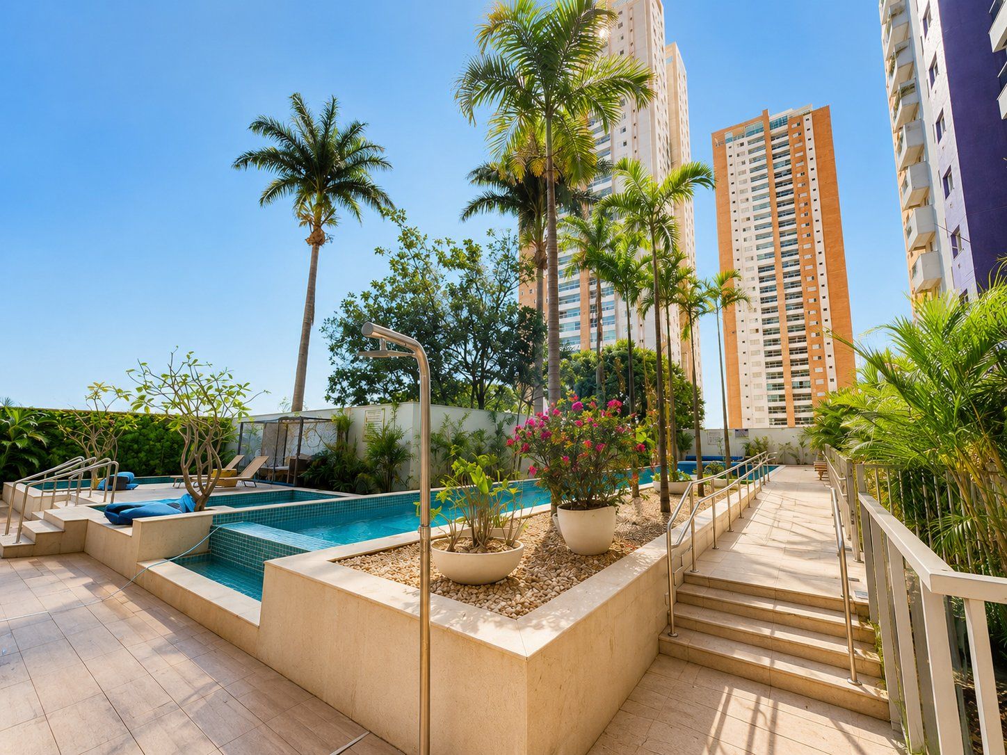 Un área de piscina en la azotea con palmeras, una piscina y una escalera que lleva a un edificio.