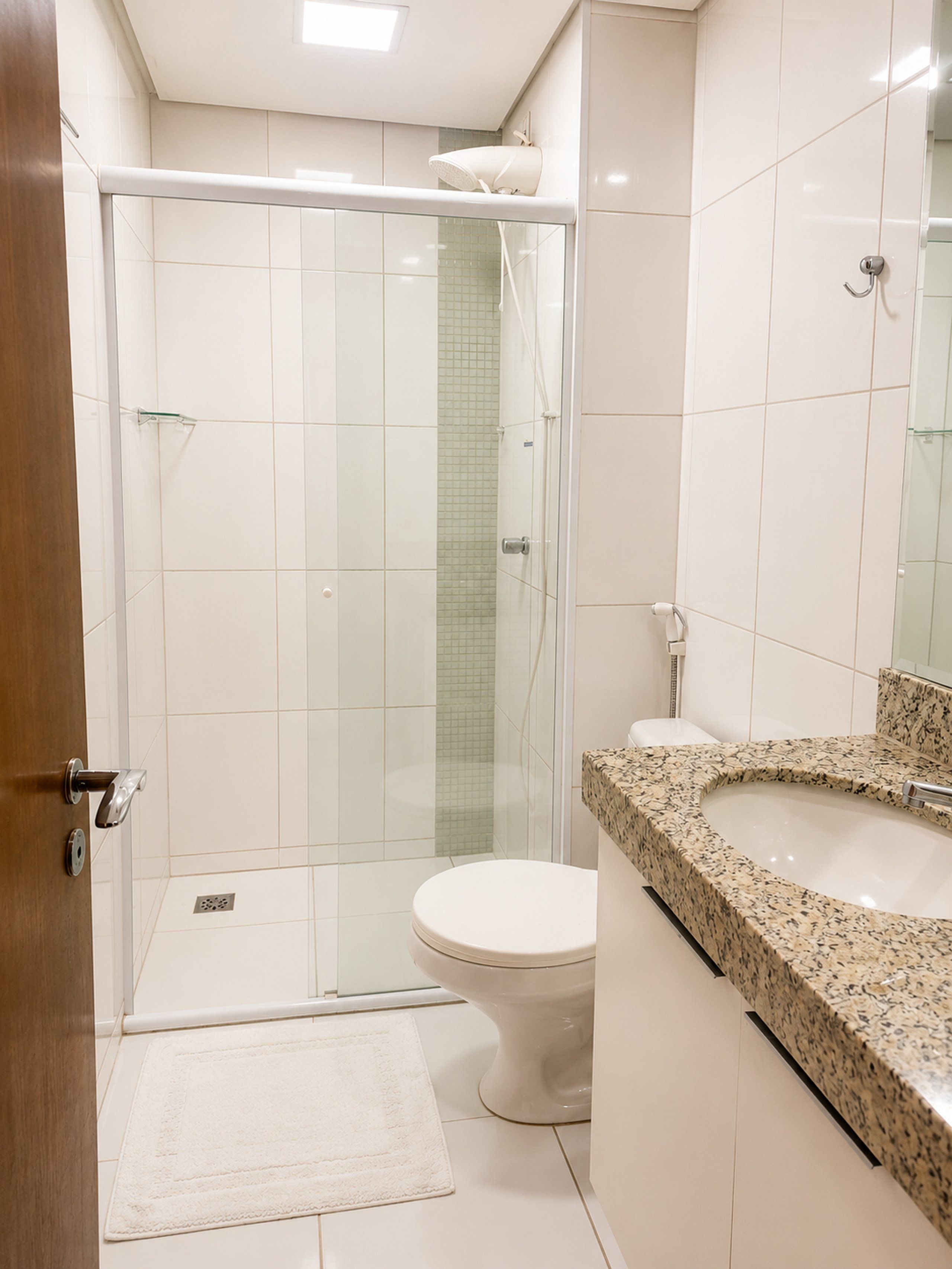 A modern bathroom with a glass-enclosed shower, a white toilet, and a granite countertop sink.
