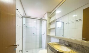 A modern bathroom with a glass shower enclosure, a granite countertop sink, and a large mirror. - The Expression 2 Quartos (Goiânia)
