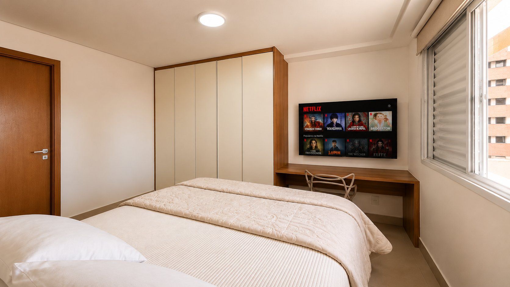 Un dormitorio con cama, escritorio y televisor de pared mostrando series de Netflix.