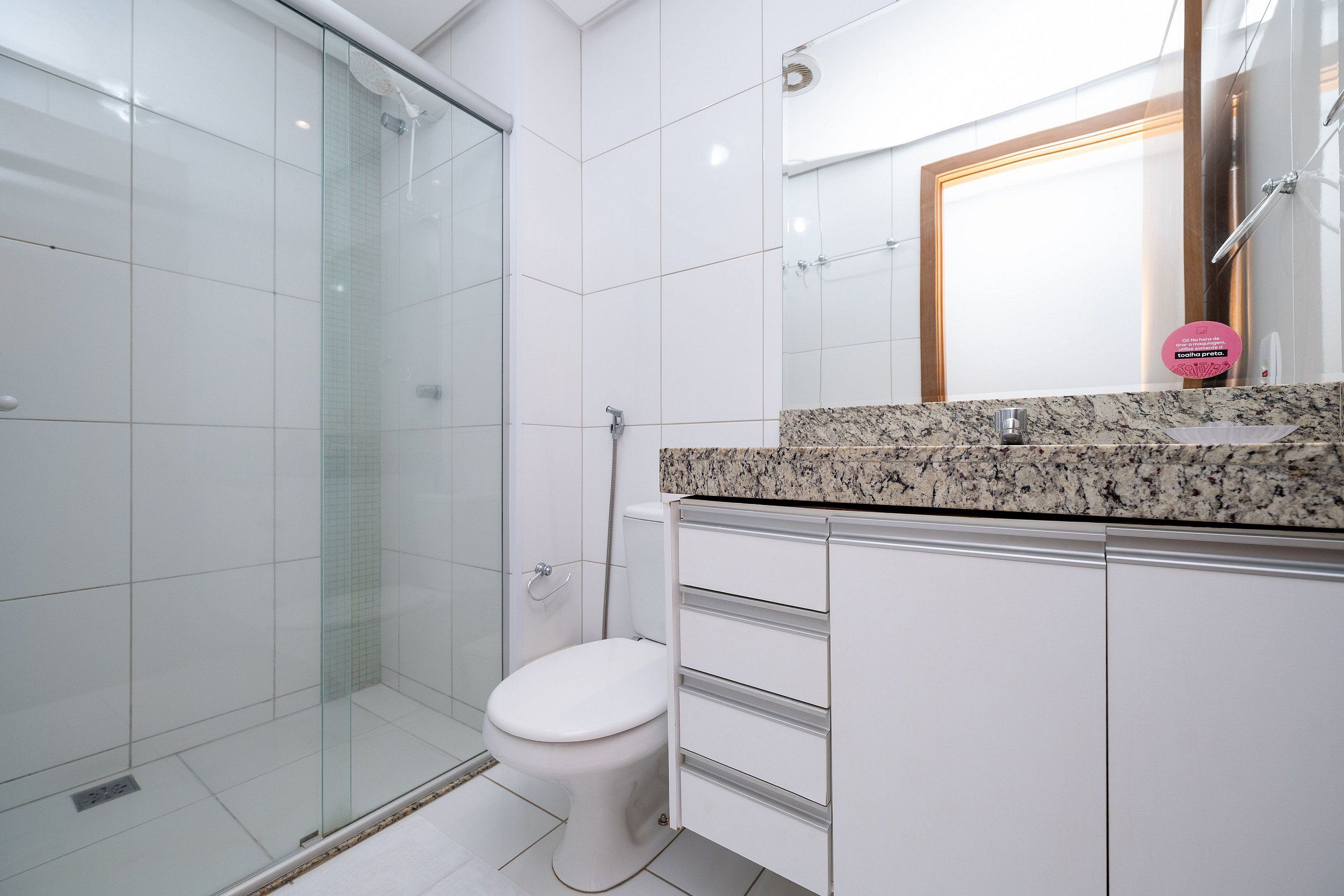 Uma casa de banho moderna com cabine de duche em vidro, sanita branca e bancada de granito com lavatório.
