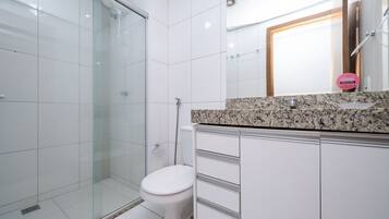 Uma casa de banho moderna com cabine de duche em vidro, sanita branca e bancada de granito com lavatório.