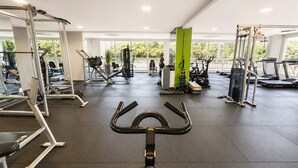 A gym with exercise equipment, a treadmill, and a green pillar. - The Expression 2 Quartos (Goiânia)